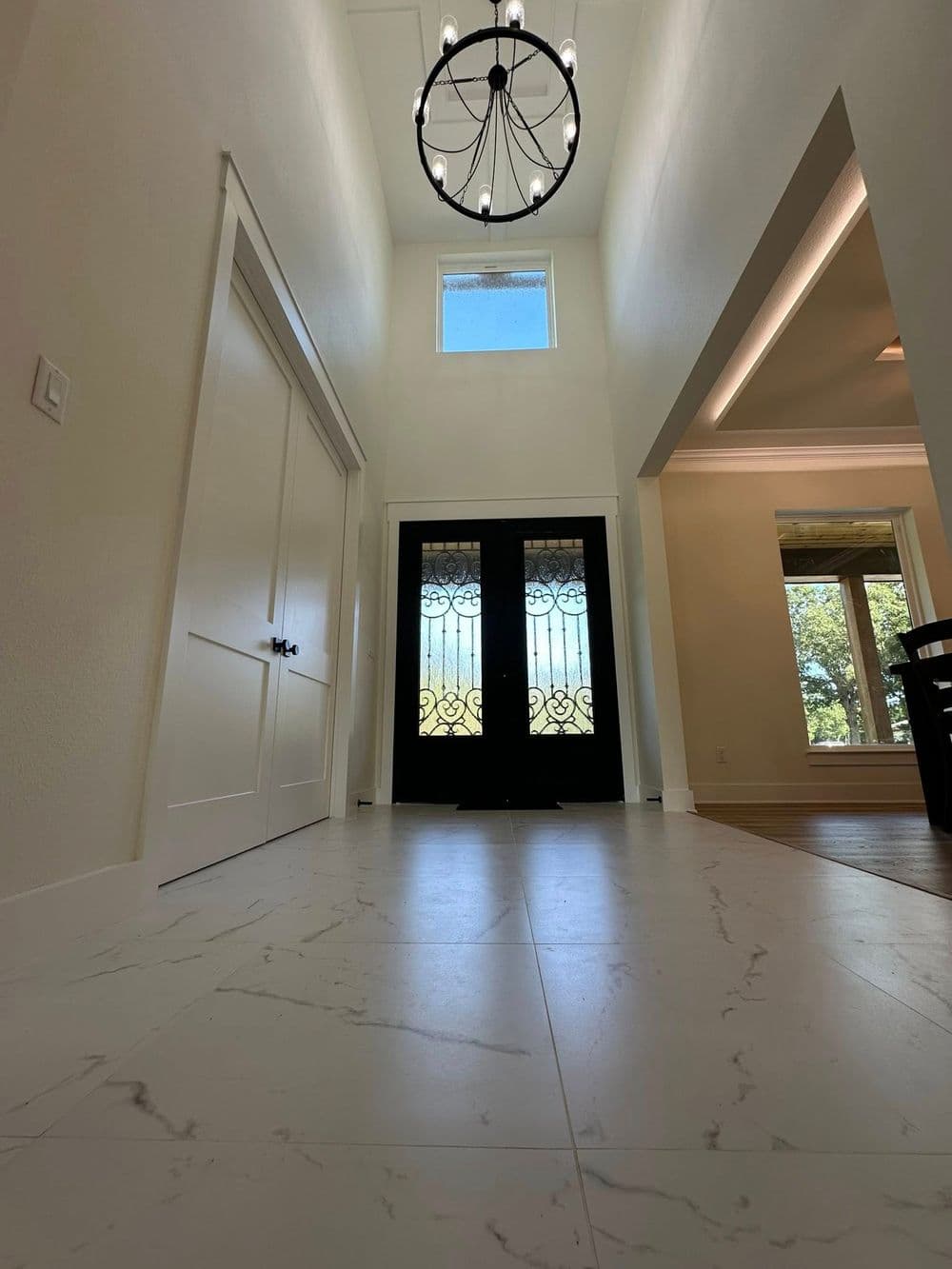 Spacious foyer with marble flooring and double front doors under a stylish chandelier.