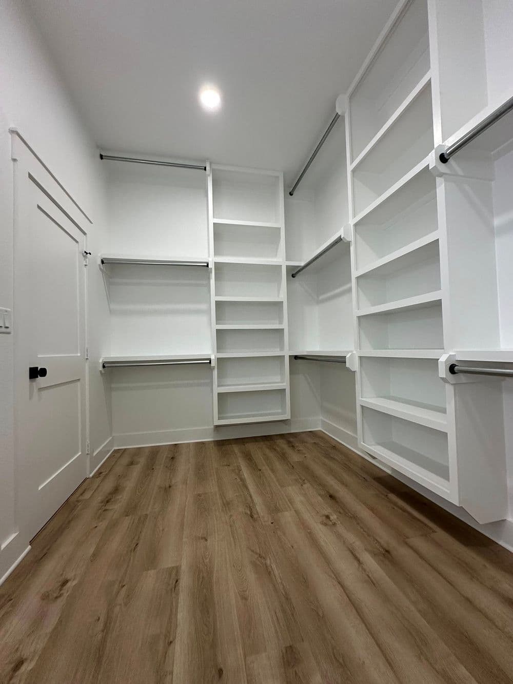 Spacious modern closet with white shelving and wooden floors, ideal for organized storage.