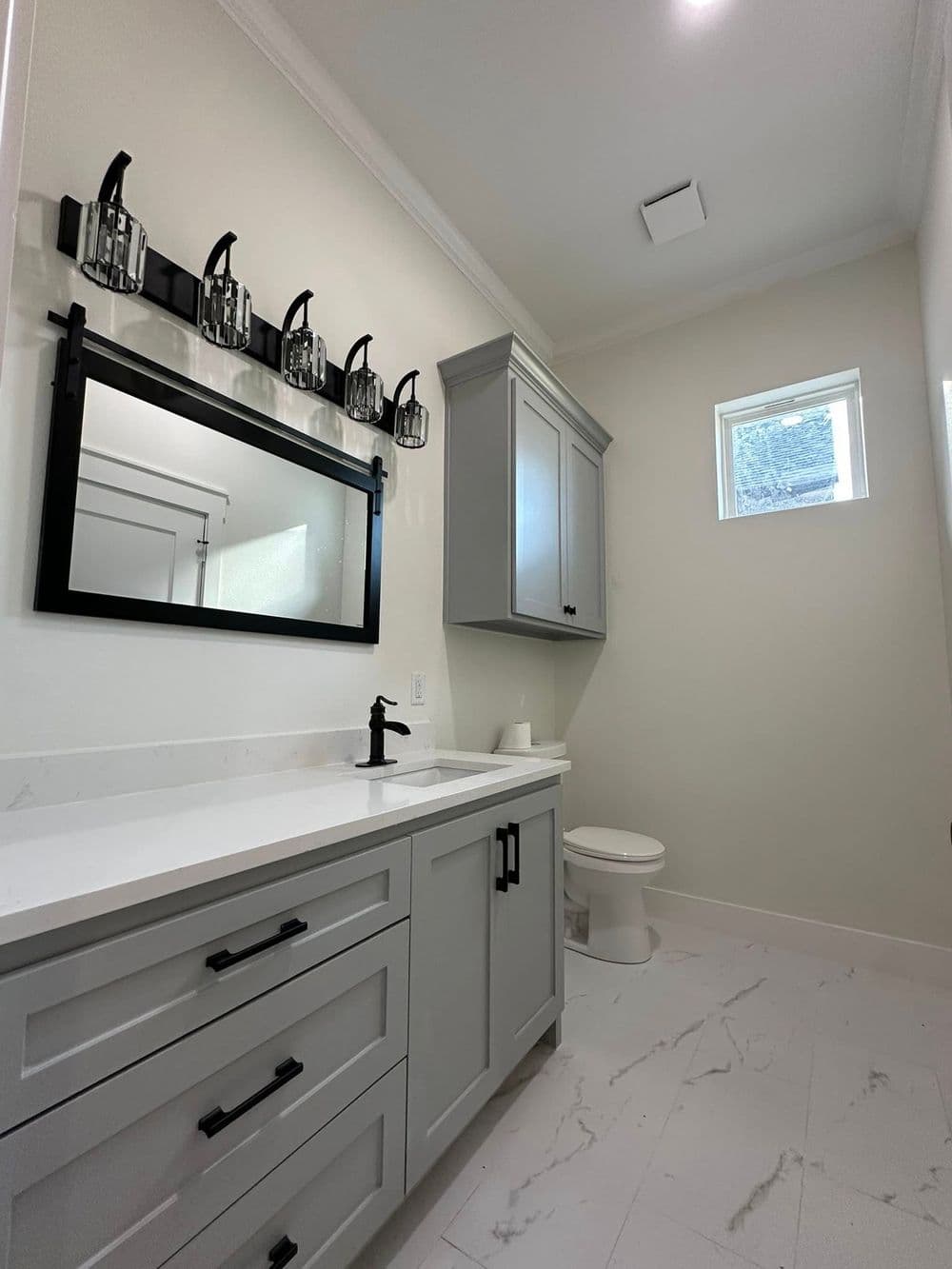 Modern bathroom with gray cabinetry, marble flooring, and stylish black fixtures.