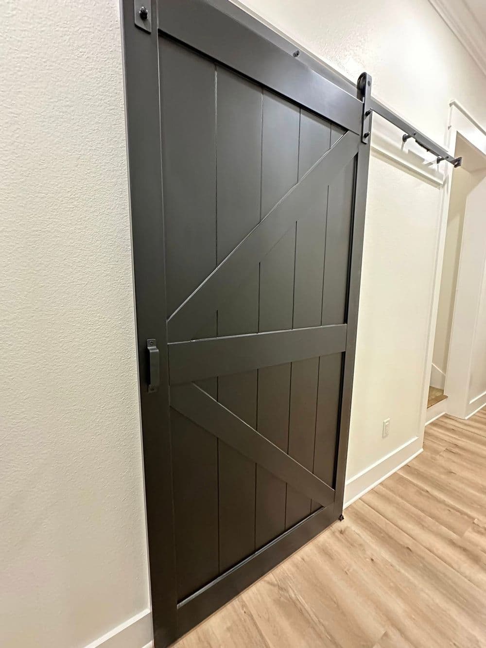 Modern dark gray barn door with wooden slats and sliding hardware inside a minimalist interior.