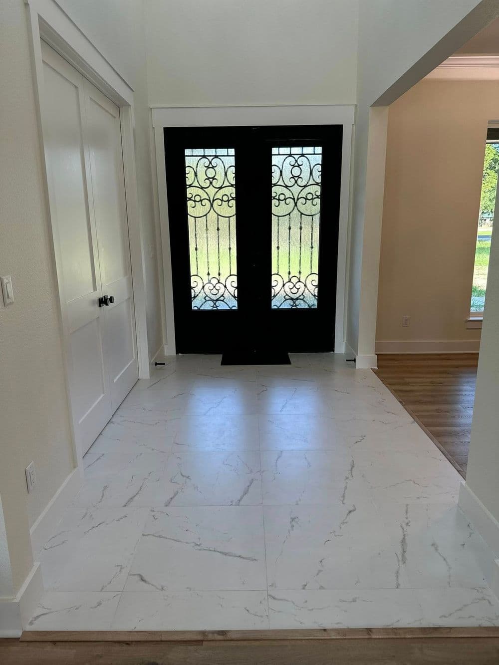 Elegant foyer with white marble floor and stylish black double doors featuring intricate designs.