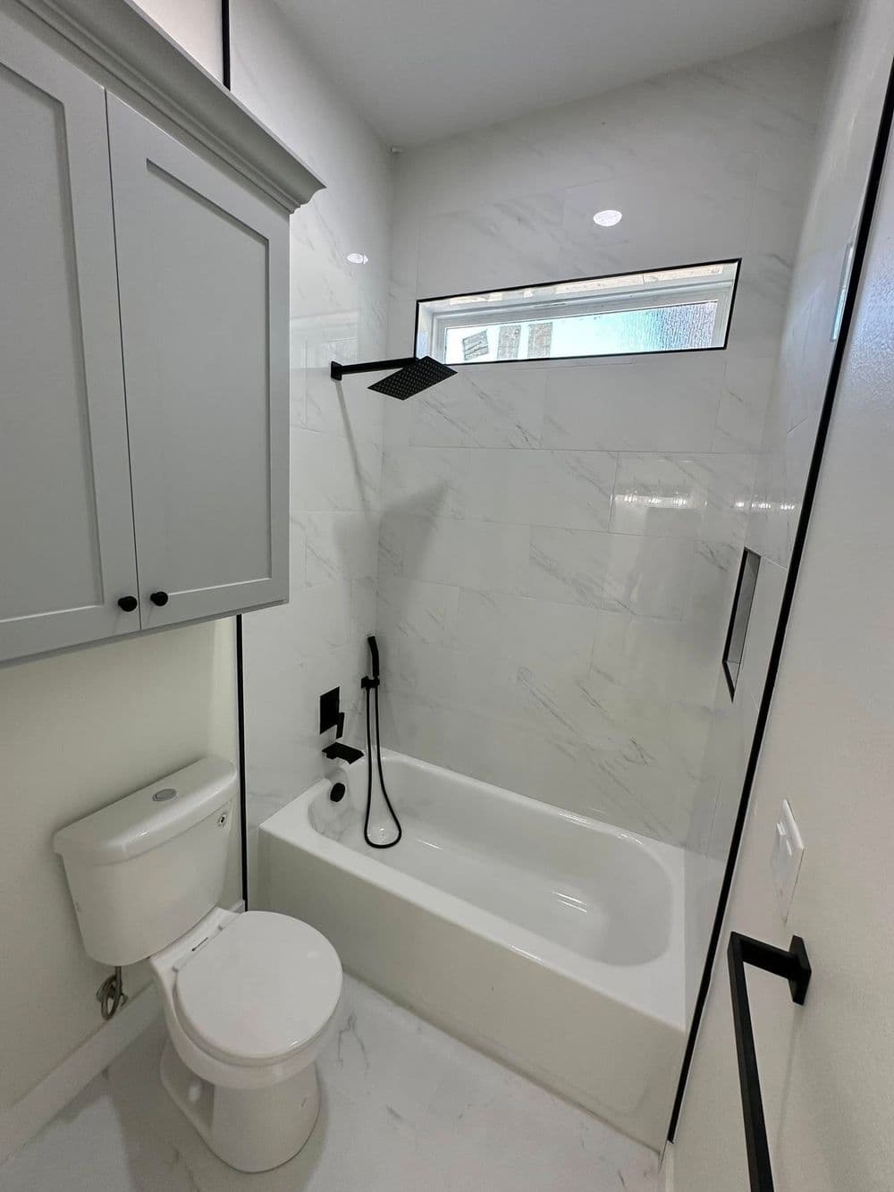 Modern bathroom featuring a tub, shower head, and sleek gray cabinetry against marble walls.
