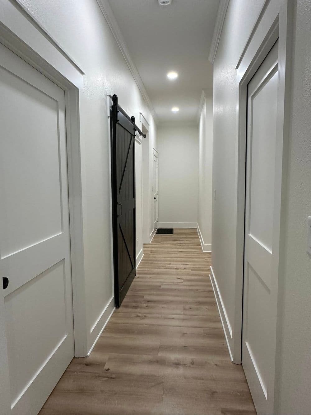 Modern hallway with light wood flooring, white walls, and a sliding barn door.