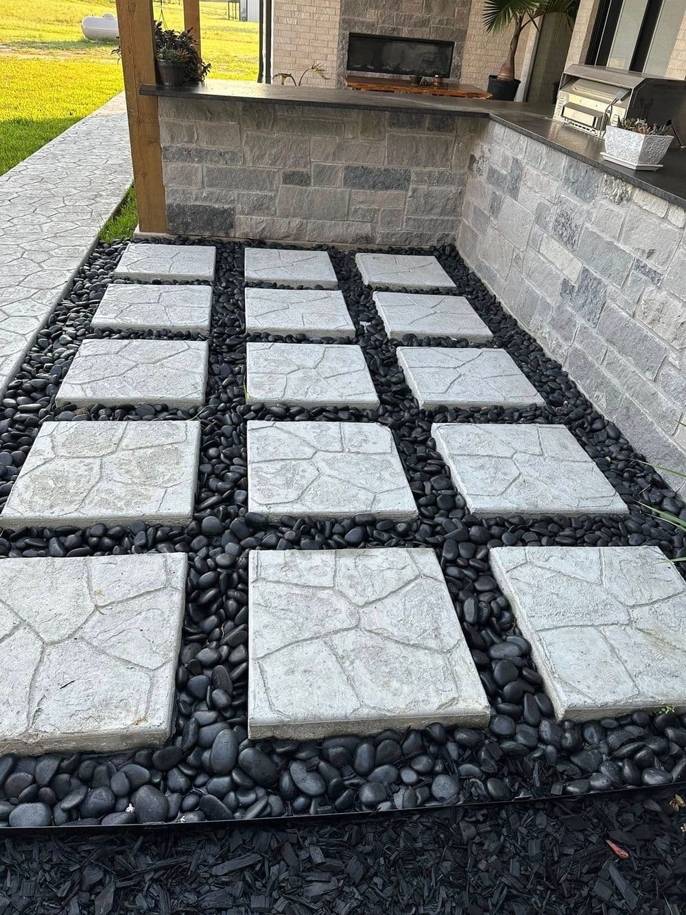 Stone pathway with concrete slabs on black pebbles, leading to an outdoor kitchen area.